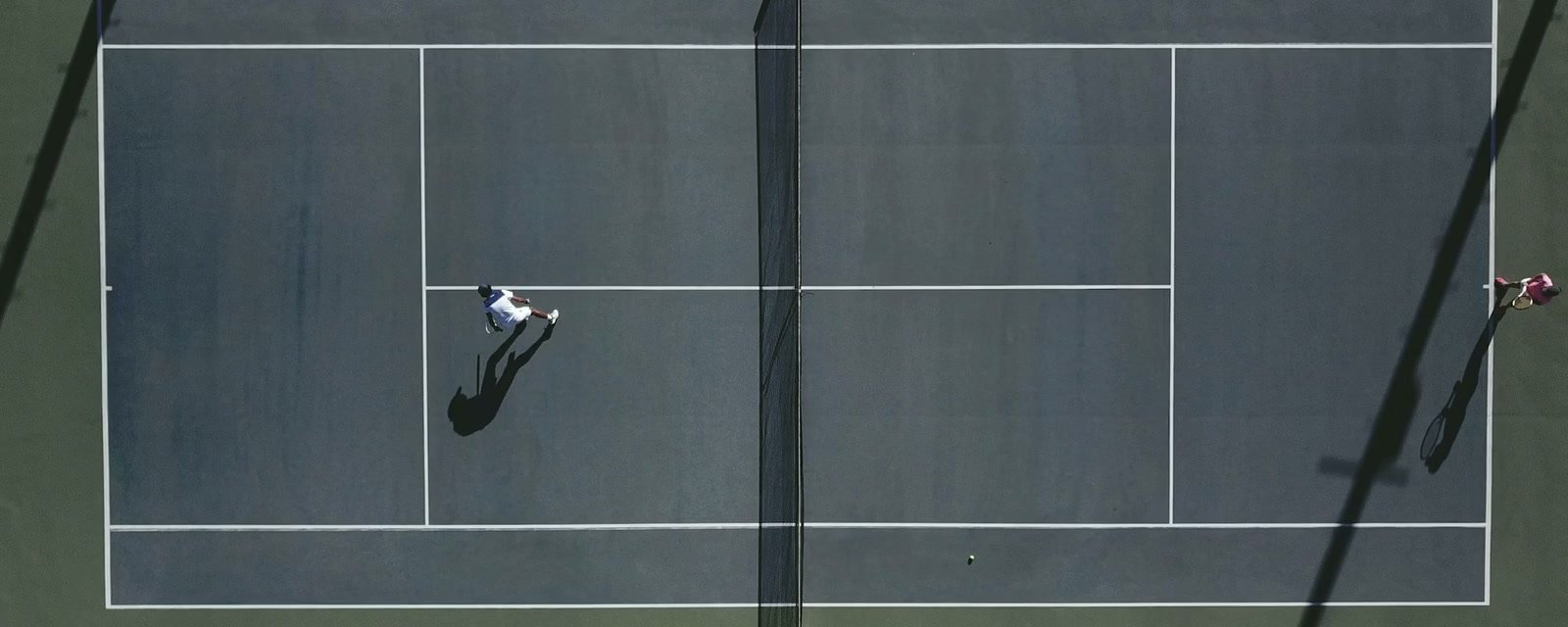 Players and long shadows seen from above a tennis court